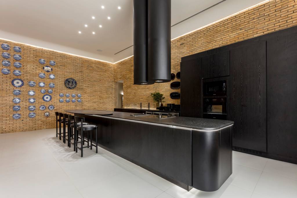 moveis-planejados-living-area-gourmet-quarto-dell-anno-marlon-gama-01 Cozinha com móveis planejados, marcenaria preta, ilha com coifa e parede com revestimento de tijolinhos.