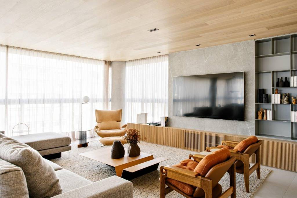 paineis-madeira-revestem-teto-escondem-portas-ape-220-m2-tres-arquitetura-credito-fran-parente (5) Painéis de madeira revestem o teto e escondem portas neste apê de 220 m². Projeto Très Arquitetura. Na foto, sala com poltronas terracorta, estante cinza e parede de madeira.