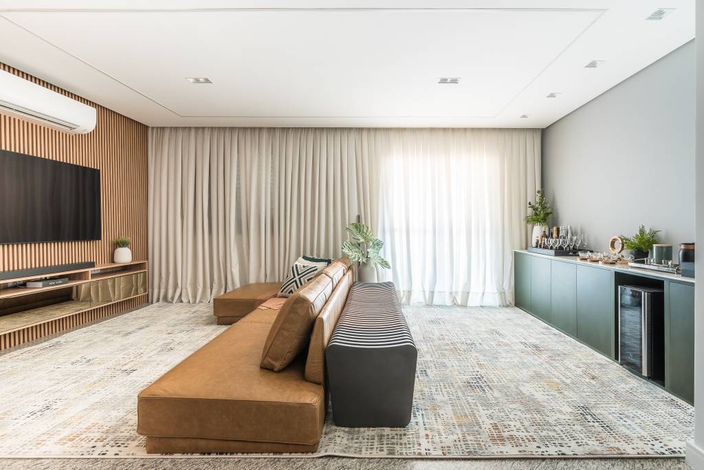 painel-de-madeira-ripada-destaque-area-social-ape-120m-clareira-arquitetura-04-sala-tapete-cortina Projeto de Clareira Arquitetura. Na foto, sala de estar com painel ripado, sofá de couro e cortina. Buffet verde com home bar.