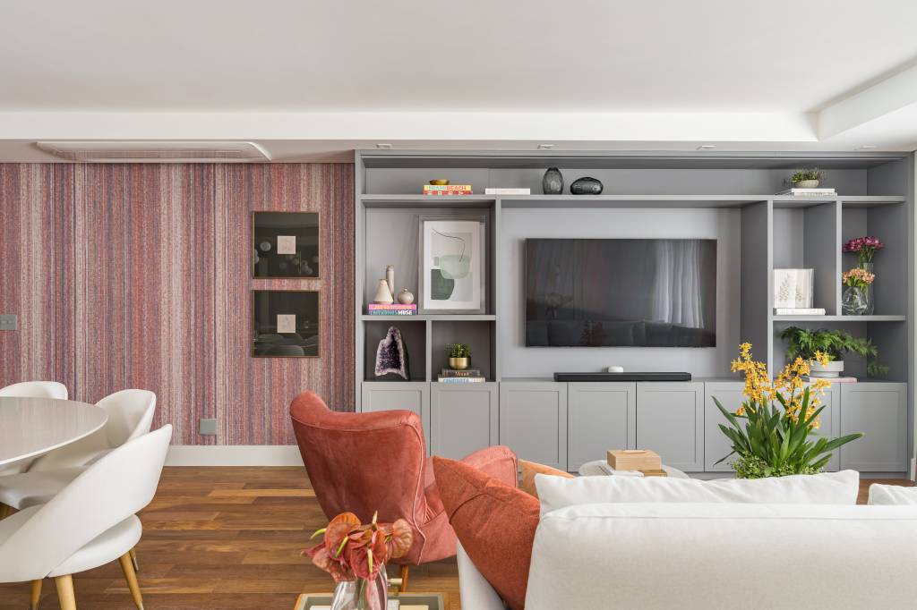 reforma-cria-suite-closet-integrado-spaco-interior-02-sala-estante Sala de estar com piso de madeira, papel de parede e estante cinza com nichos. Sofá claro e poltronas laranja.