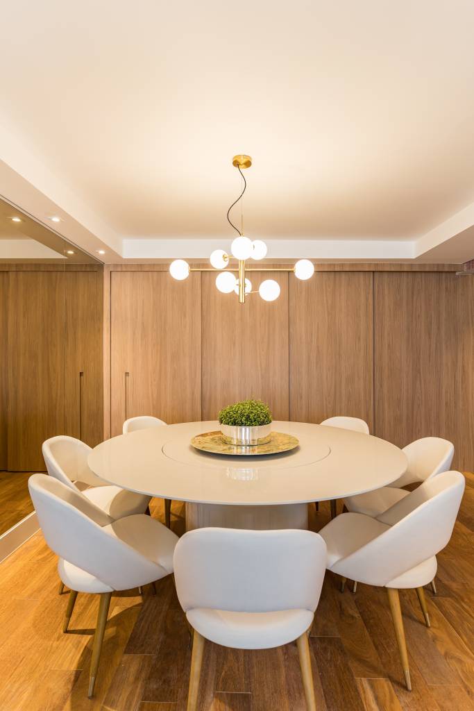 Sala de jantar com mesa redonda e cadeiras brancas. Cozinha com porta de correr ao fundo.