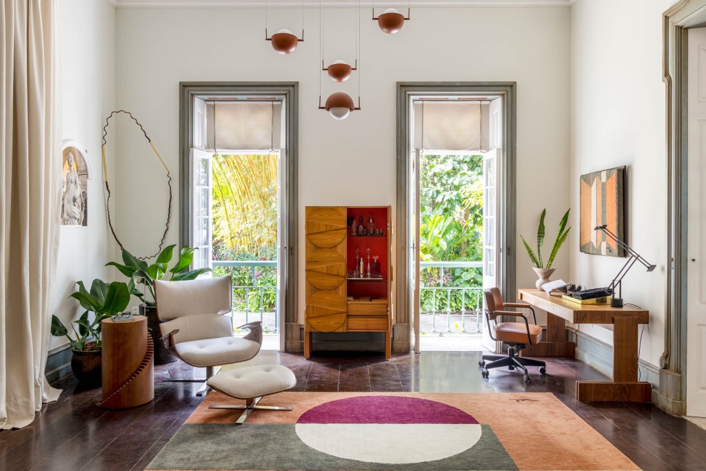 Sala de Encontros traz peças inéditas inspiradas na obra de Noel Marinho. Projeto de Patricia Marinho e Manuele Colas para a CASACOR Rio de Janeiro 2023. Na foto, sala de estar com poltrona branca e tapete. Home office e varanda.