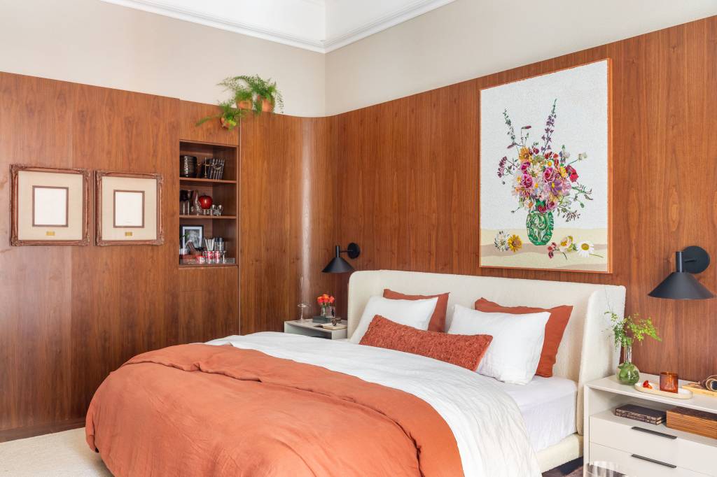 Suíte ganha conforto quarto de hotel com paredes de madeira. Projeto de Paula Muller para a CASACOR Rio 2023. Na foto, quarto com paredes de madeira e quadros.