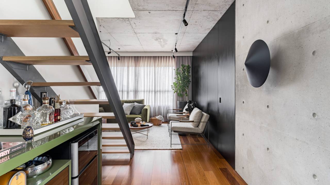 Apê de 140 m² com estilo industrial tem pia no quarto e jardim de cactos. Projeto de Gabriela Prado. Na foto, sala com escada, bar e paredes pretas.