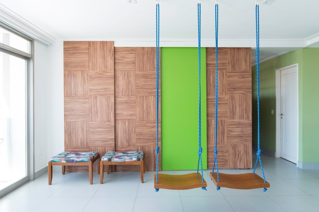 Projeto de Raízes Arquitetos. Na foto, painéis de madeira, porta verde e balanços.