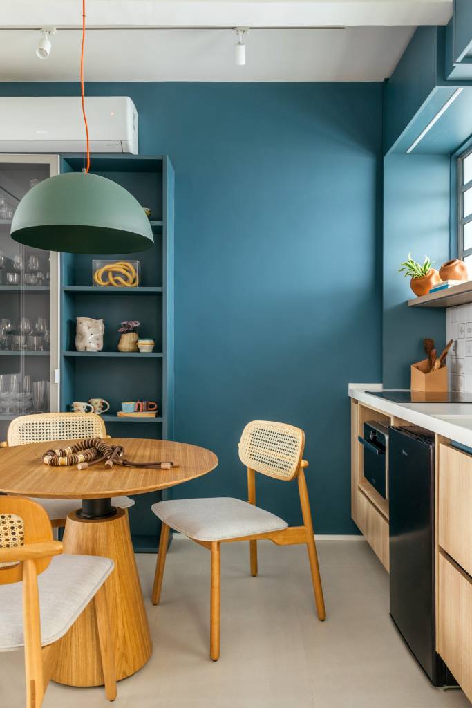 prateleira-armarios-cozinha-loft-30m-casa-cururu-01 Projeto de Casa Cururu. Na foto, cozinha pequena com parede e marcenaria azul, bancada branca, prateleira e armário emoldurando janela.