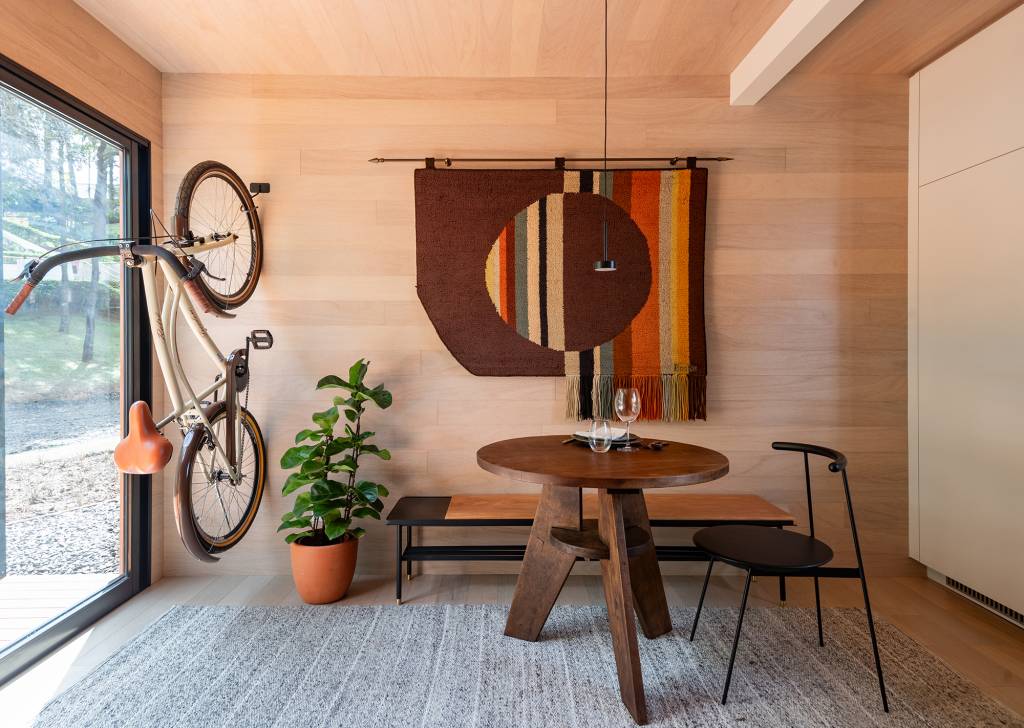 tiny-house-sustentavel-madeira-pronta-em-1-mes-credito-favaro-jr (23) Tiny house sustentável de madeira fica pronta em 1 mês. Na foto, sala de jantar com tapecaria na parede e bicicleta.