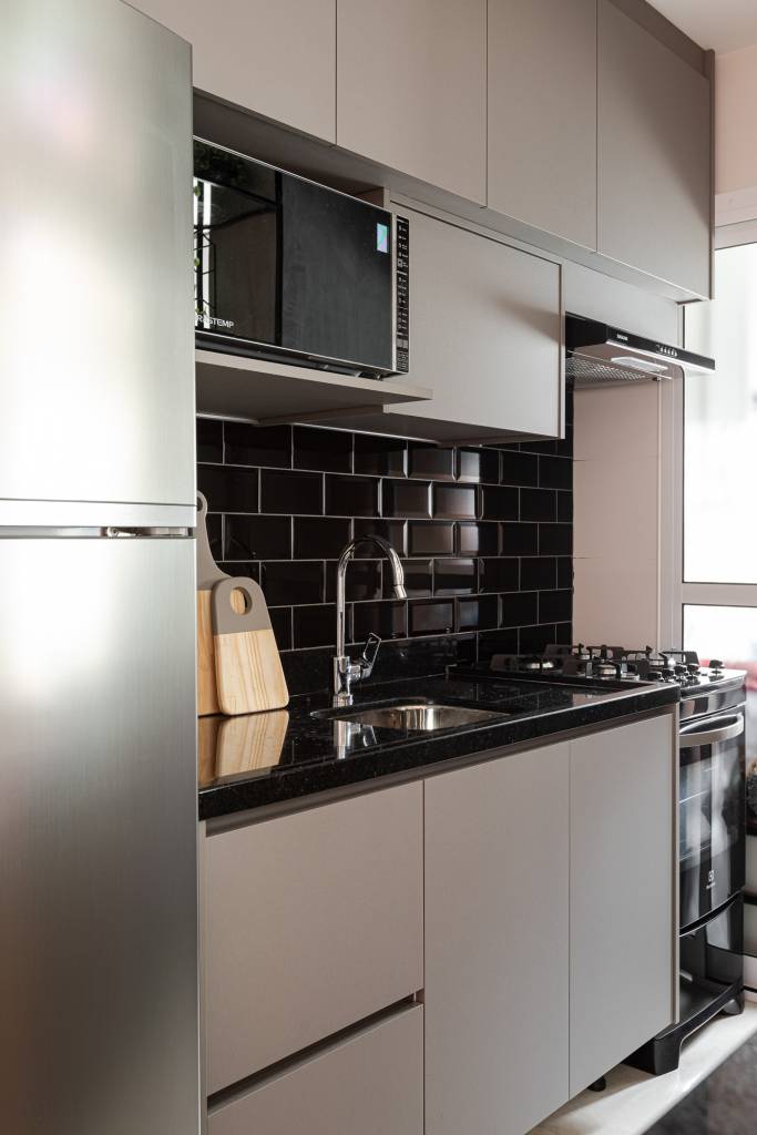 tons-rosa-verde-ape-inspirado-em-gossip-girl-inovando-arquitetura-19-cozinha-preta Projeto de Inovando Arquitetura. Na foto, cozinha com marcenaria cinza clara, bancada preta e backsplash de tijolinhos pretos.