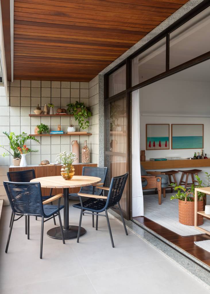 vibrante-atemporal-tons-verde-azul-ape-140m-maia-romeiro-arquitetura-05-varanda-plantas Projeto de MR Arquitetura. Na foto, varanda com mesa pequena redonda, cadeiras azuis e parede de azulejos com prateleiras com plantas.