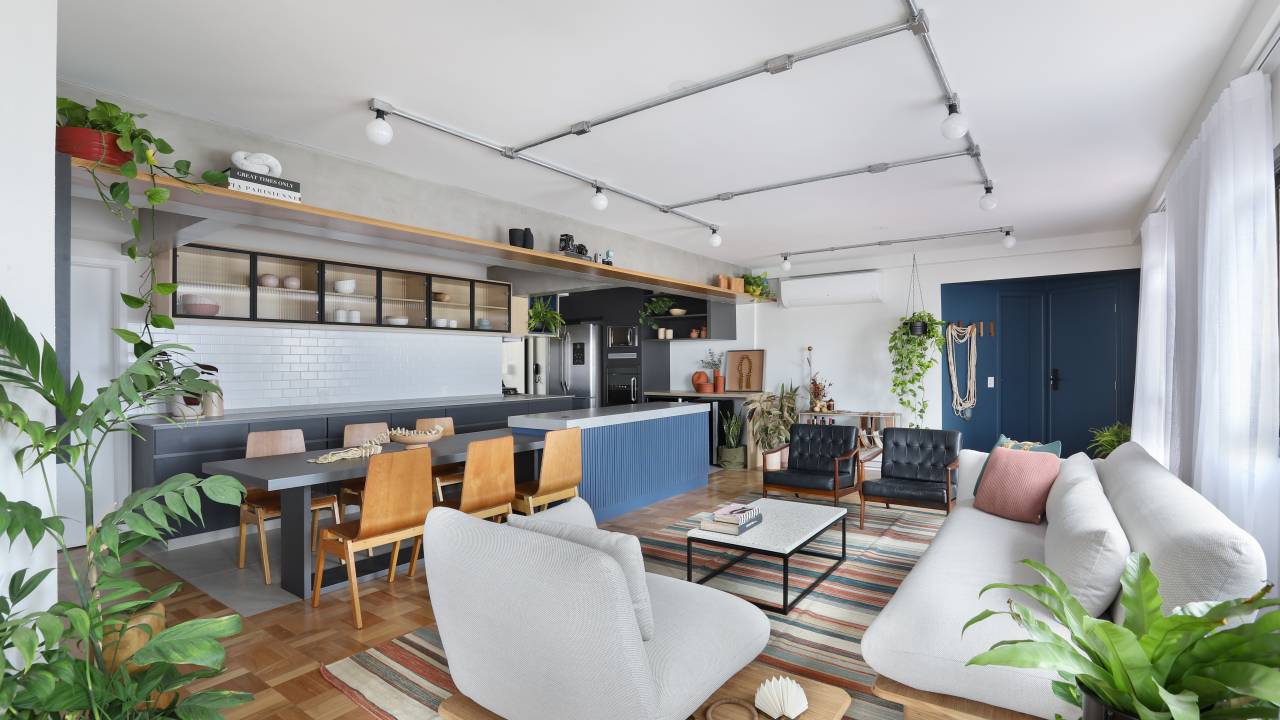 Apê de 180m² ganha color block azul na entrada e área de descompressão. Projeto de Studio 92 Arquitetura. Na foto, sala de estar integrada com cozinha com piso de taquinho e tapete colorido.