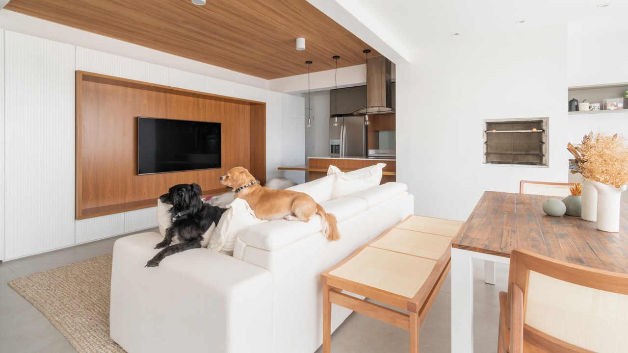 Apê minimalista de 100 m² foi pensado para os quatro cachorros da família. Projeto de Entre Studio. Na foto, varanda com espaço gourmet. poltrona de leitura e sala integrada.