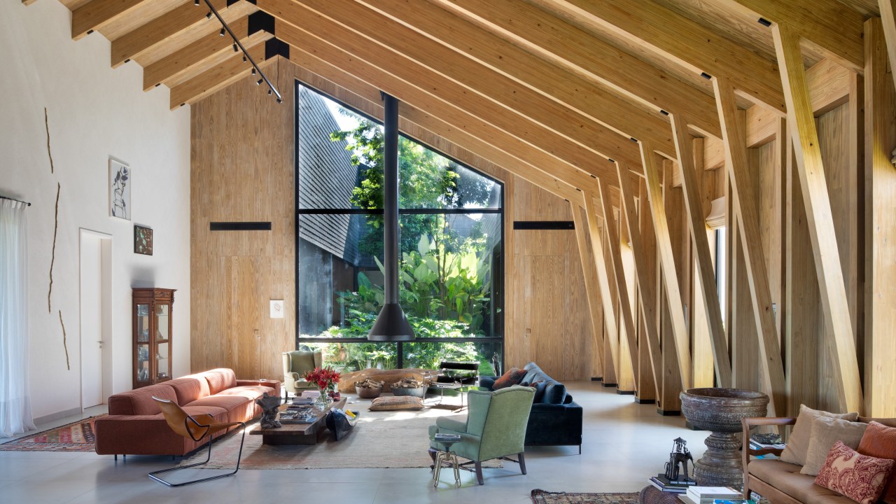 Casa celeiro de madeira une o rústico e o moderno em projeto de 1230 m². Projeto de Otto Felix. Na foto, sala de estar com paredes de madeira, lareira e vista para o jardim.