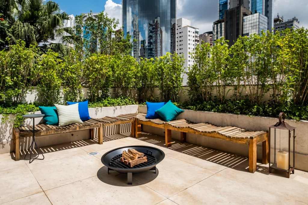 Ôfuro, área gourmet e lareira compõem este apartamento garden de 173 m². Projeto de Ocanhas Arquitetura e Sandra Steuer Arquitetura. Na foto, terraço com bancos e jardineiras e fogo de chão.