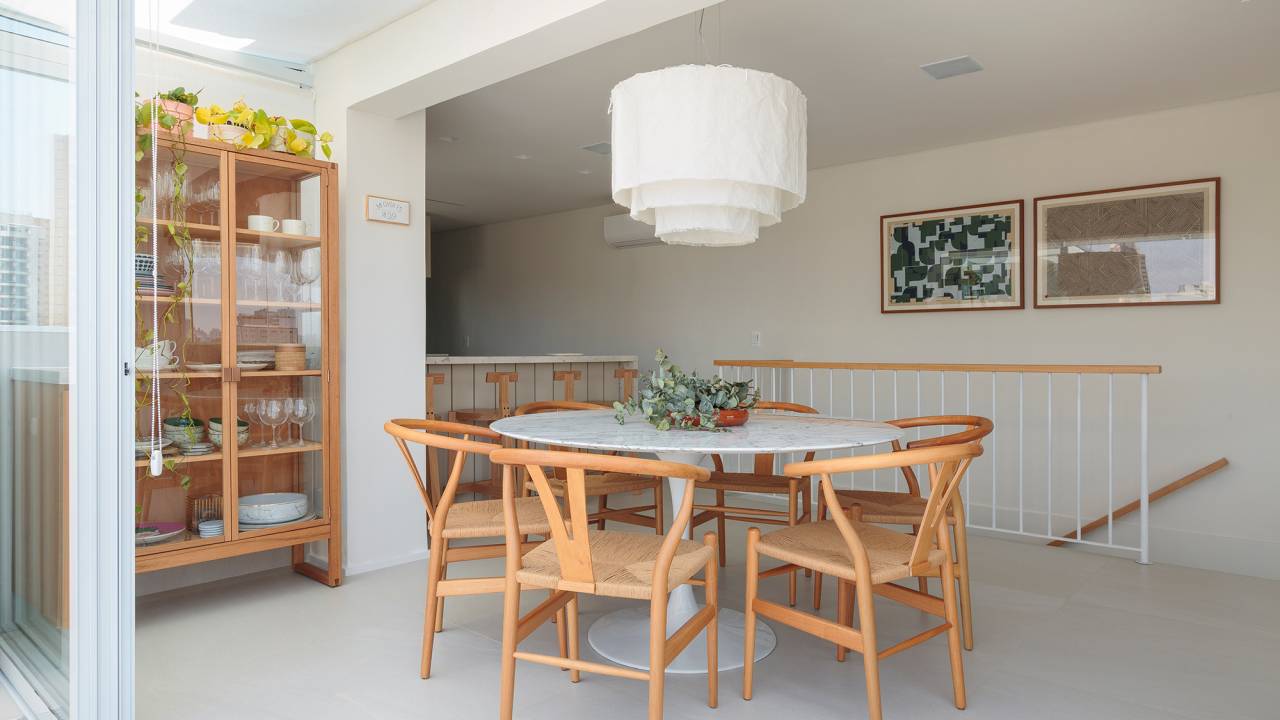 Tons neutros e espaço gourmet ao ar livre marcam este apê de 140 m². Projeto do Estudio Maré. Na foto, sala de jantar com cristaleira e quadros.