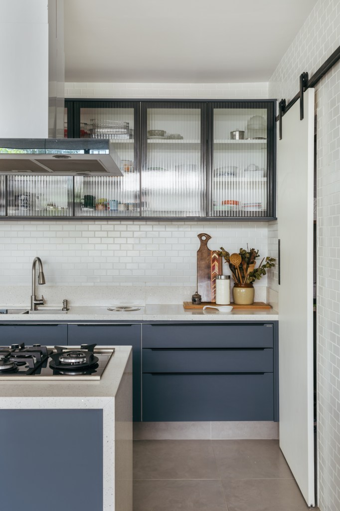 Casa de casal de 70 anos apaixonado por samba inspira-se na brasilidade. Projeto de Ana Cano. Na foto, bancada de cozinha branca, marcenaria azul e backsplash de subway tiles.