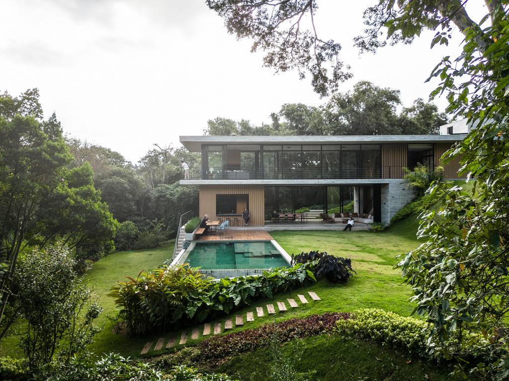 Casa de campo imersa na natureza parece flutuar em meio ao verde. Projeto de Conrado Ceravolo. Na foto, fachada da casa em meio ao jardim. Piscina e varanda.