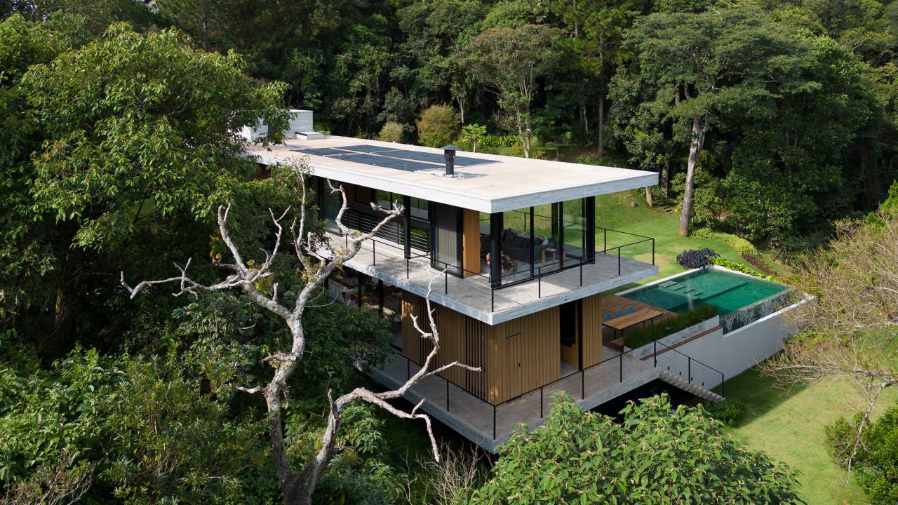 Casa de campo imersa na natureza parece flutuar em meio ao verde. Projeto de Conrado Ceravolo. Na foto, fachada da casa em meio ao jardim. Piscina e varanda.