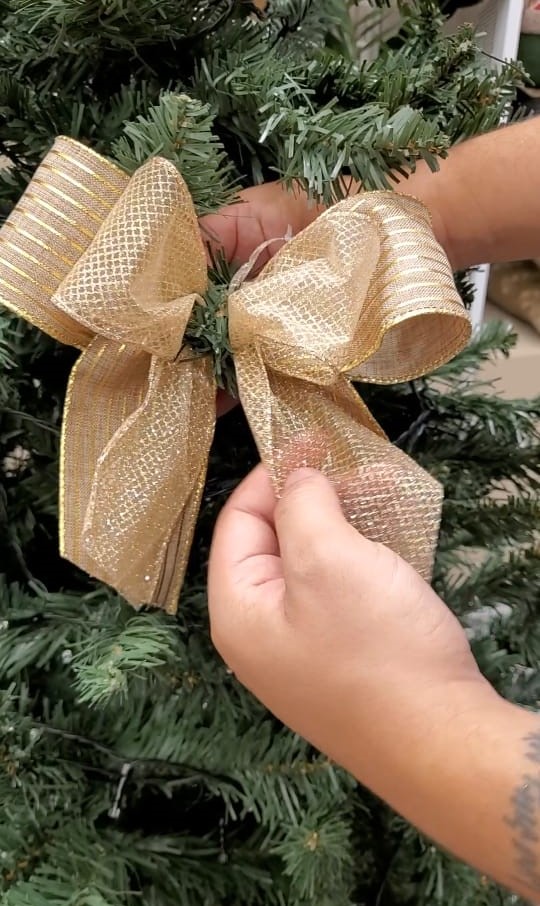 Passo a passo para montar uma Árvore de Natal igual às do shopping. Na foto, laço sendo colocado na árvore.