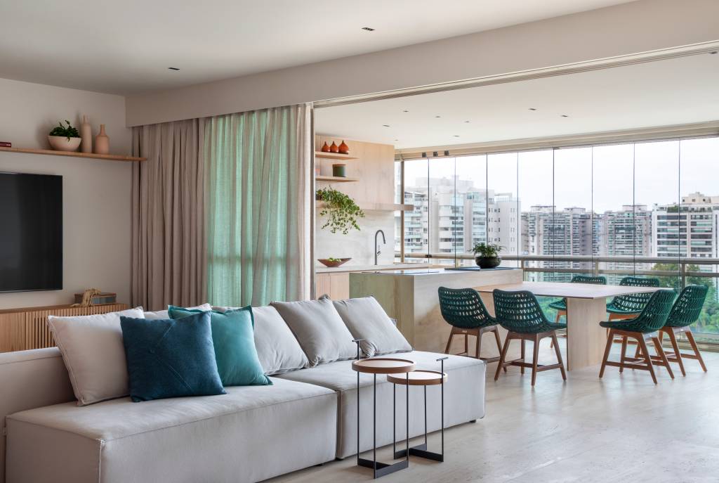 Varanda gourmet espaçosa com ilha travertino natural é destaque em apê