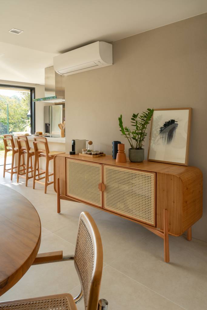 Palhinha, madeira e pedras dão toque boho a esta casa de 130m². Projeto de NOSSA Casa Arquitetura. Na foto, buffer com porta de palhinha com vaso com planta e quadro. Ar condicionado.