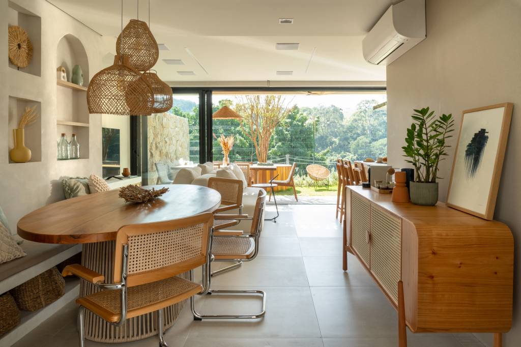 Palhinha, madeira e pedras dão toque boho a esta casa de 130m². Projeto de NOSSA Casa Arquitetura. Na foto, sala de jantar integrada com porta de vidro para jardim e luminária de palhinha.