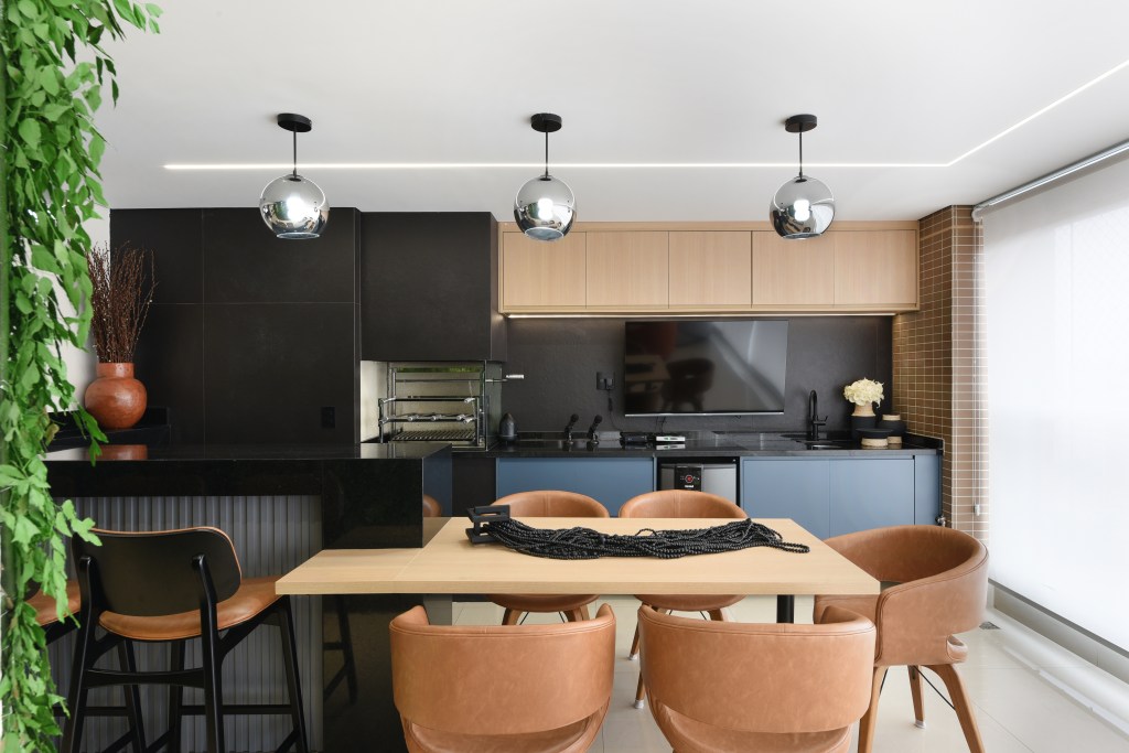 Reforma em apê de 204m² cria área gourmet com mix de granito e MDF. Projeto de AB Palacios Arquitetura. Na foto, área gourmet com marcenaria azul, bancada e mesa com cadeiras estofadas.