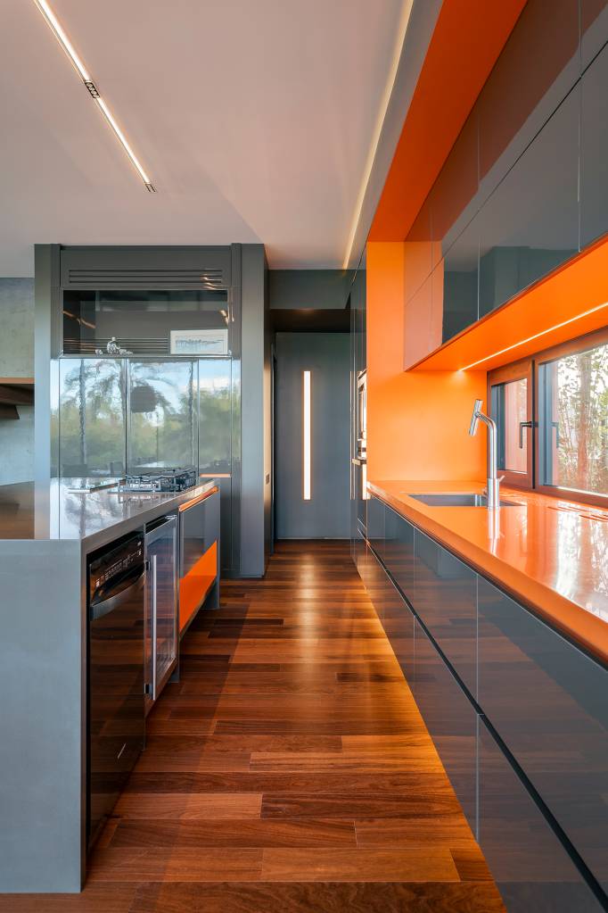A água é destaque nesta casa de 457 m² no Rio Grande do Sul. Projeto de Stemmer Rodrigues. Na foto, cozinha com revestimentos laranja e cinza.