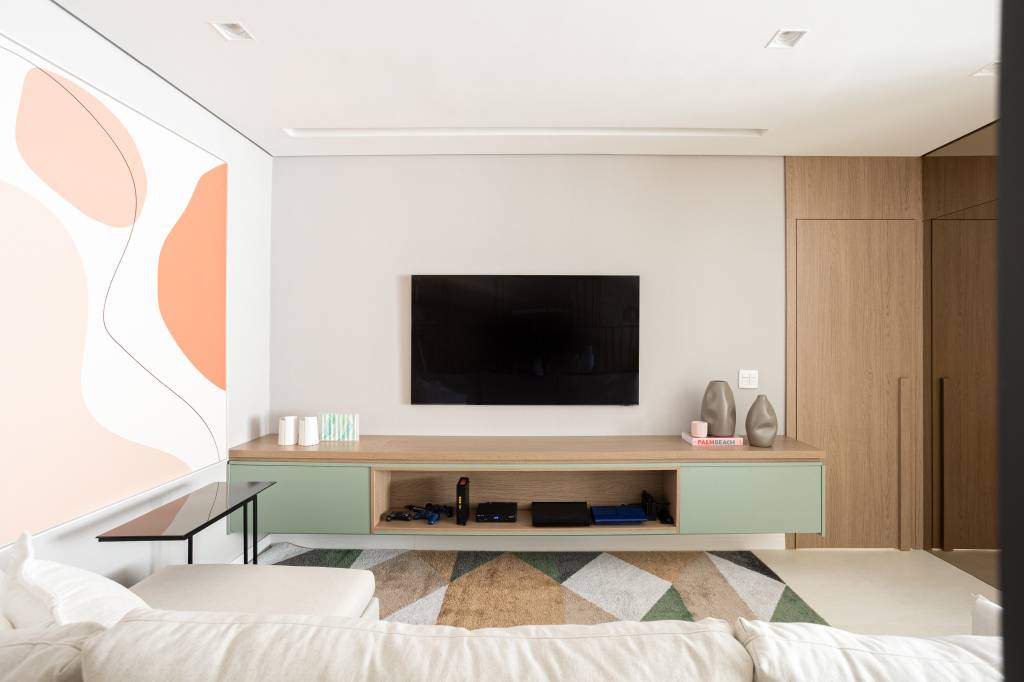 apartamento-140-m2-parede-pedra-moledo-quarto-montessoriano-loft7-arquitetura (6) Apartamento de 140 m² possui parede de pedra moledo e quarto montessoriano. Projeto Loft 7 Arquitetura. Na foto, sala de tv com tapete colorido e quadro.
