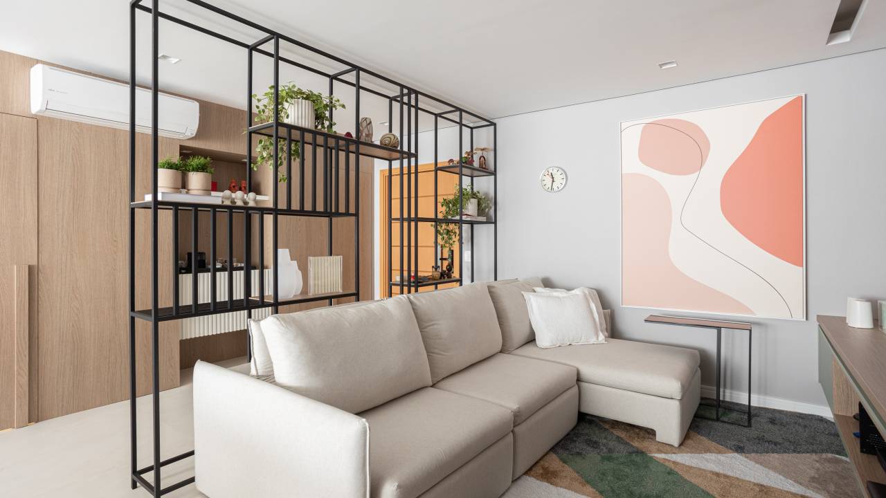 Apartamento de 140 m² possui parede de pedra moledo e quarto montessoriano. Projeto Loft 7 Arquitetura. Na foto, sala de TV com estante de serralheria e tapete colorido.