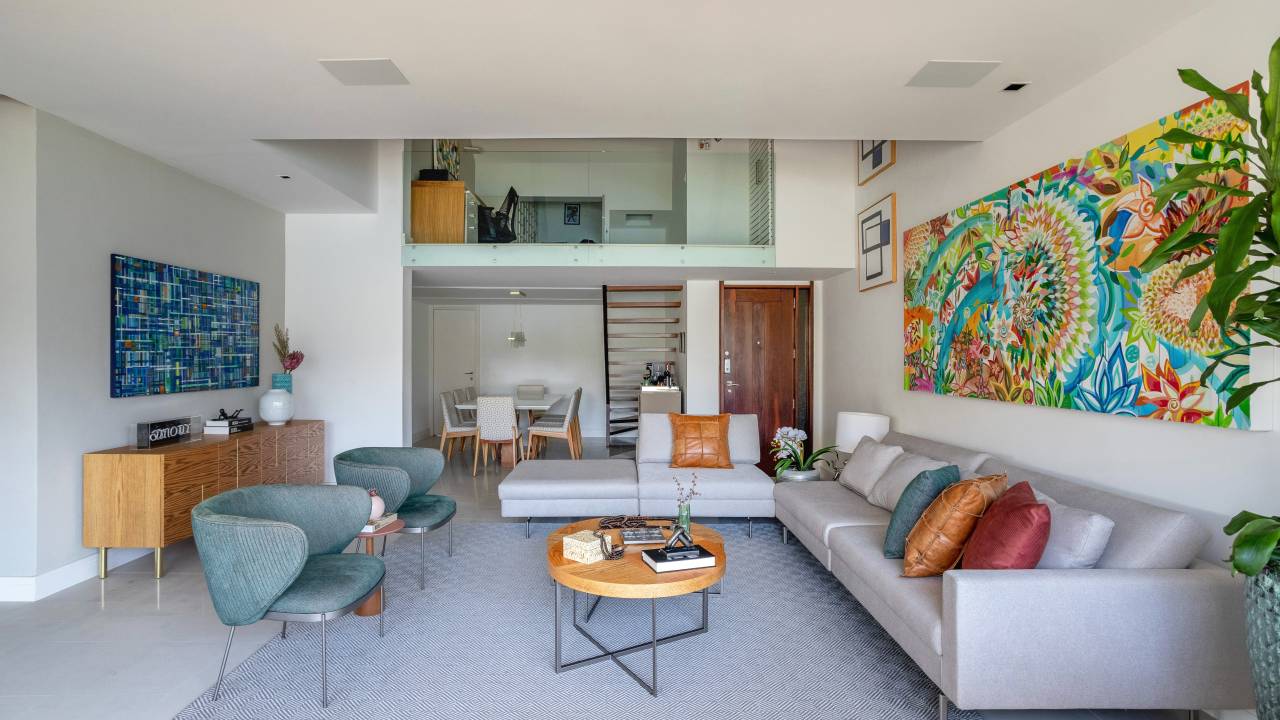 Apê ganha mezanino com home office, lavabo azul e copa de cozinha turquesa. Projeto de Ana Cano Arquitetura. Na foto, sala de estar, poltrona verde, quadro colorido e mezanino.