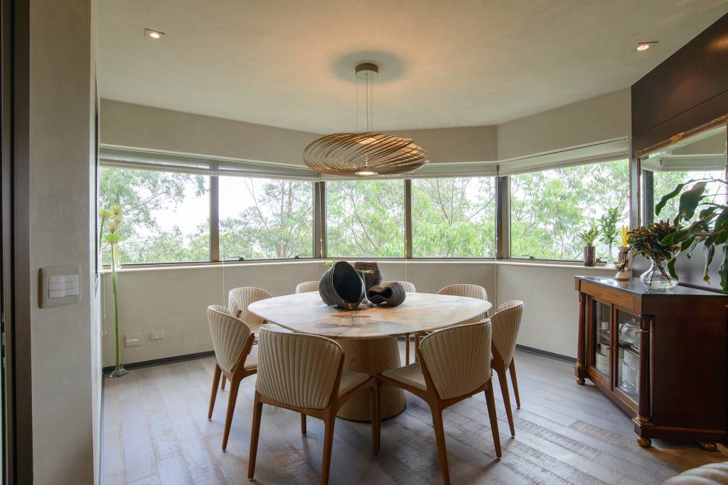 Painéis de madeira escura caracterizam o projeto deste apê de 250 m². Projeto de Andrea Parreira Arquitetura. Na foto, sala de jantar com mesa redonda e vista para as árvores.