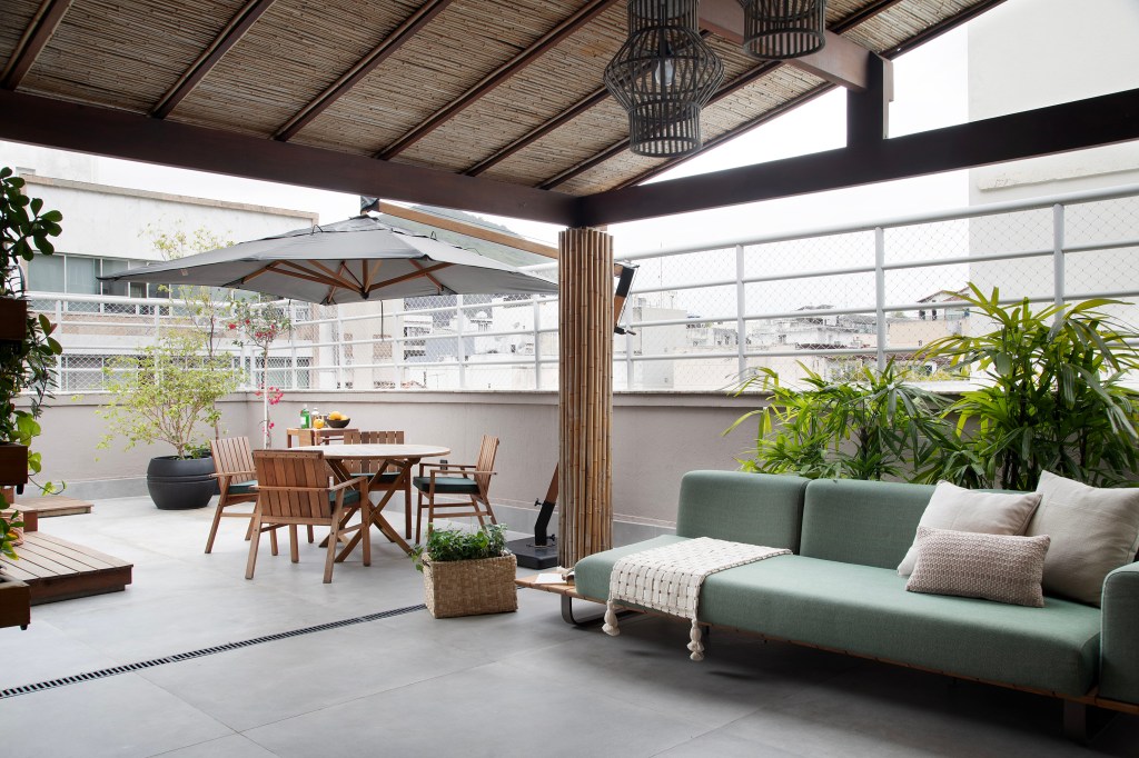 Com paleta sóbria, cobertura ganha cozinha cinza e sala íntima. Projeto de Travessa Arquitetura. Na foto, cobertura com pergolado, ombrelone e sofá verde.