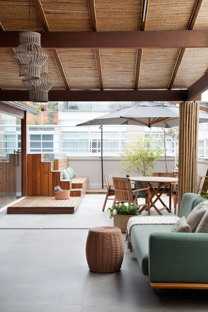 Com paleta sóbria, cobertura ganha cozinha cinza e sala íntima. Projeto de Travessa Arquitetura. Na foto, cobertura com pergolado, ombrelone e sofá verde.