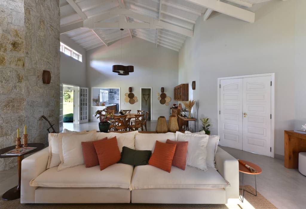 Rústico chic: casa de campo tem orquidário e cozinha com cara de fazenda. Projeto de Rosangela Pena. Na foto, sala de estar com pé direito alto, lareira, sofá branco e poltronas.