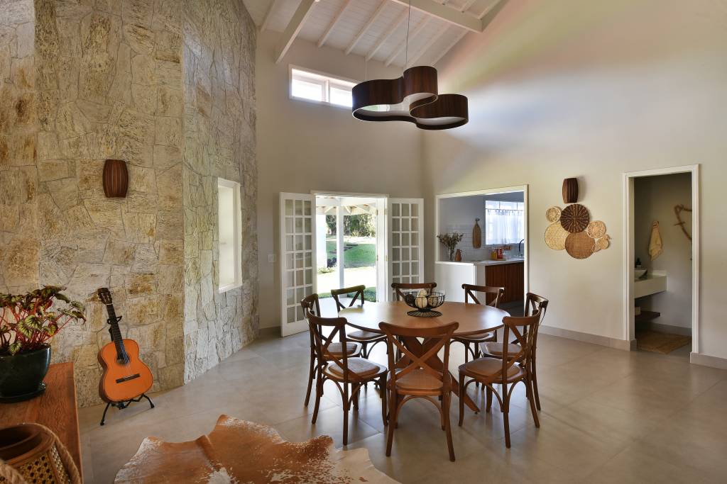 Rústico chic: casa de campo tem orquidário e cozinha com cara de fazenda. Projeto de Rosangela Pena. Na foto, sala de jantar com pé direito duplo, mesa redonda de madeira e luminária.