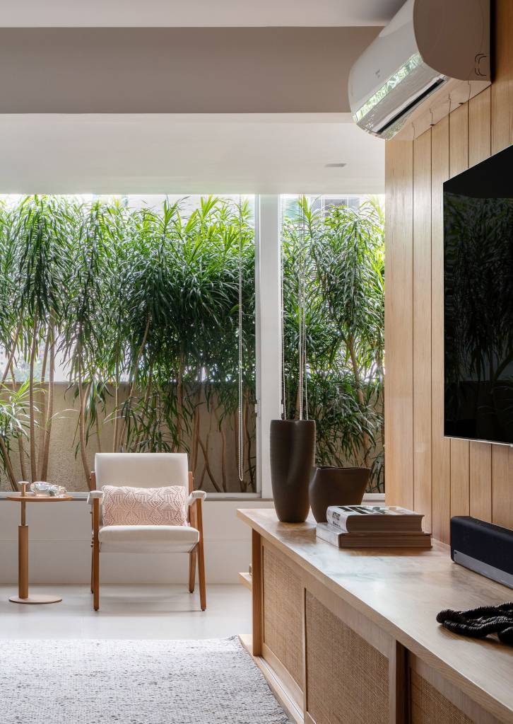 Sala de apê tem janela do piso ao teto para o terraço com jardineira. Projeto de Ao Quadrado Arquitetura. Na foto, sala de estar, poltronas brancas, sofá cinza escuro, plantas na varanda.