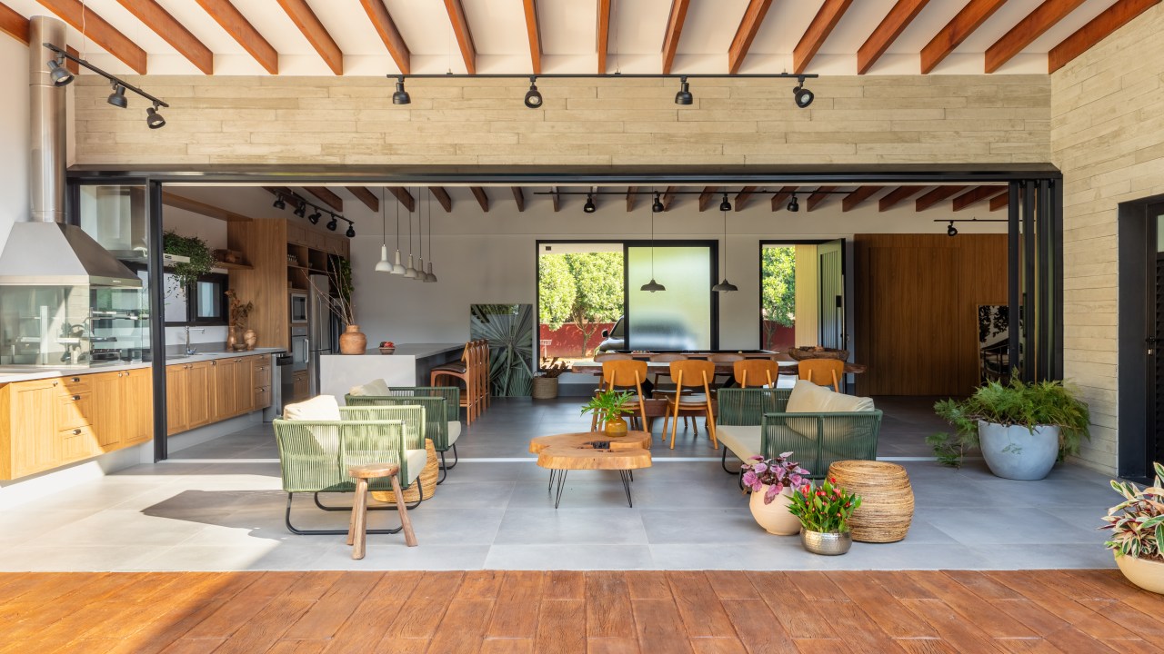 Com sala de jogos e área gourmet ampla, casa de campo vira lar permanente. Projeto de Pietro Terlizzi Arquitetura. Na foto, área gourmet com bancada branca, sofás para área externa, churrasqueira.