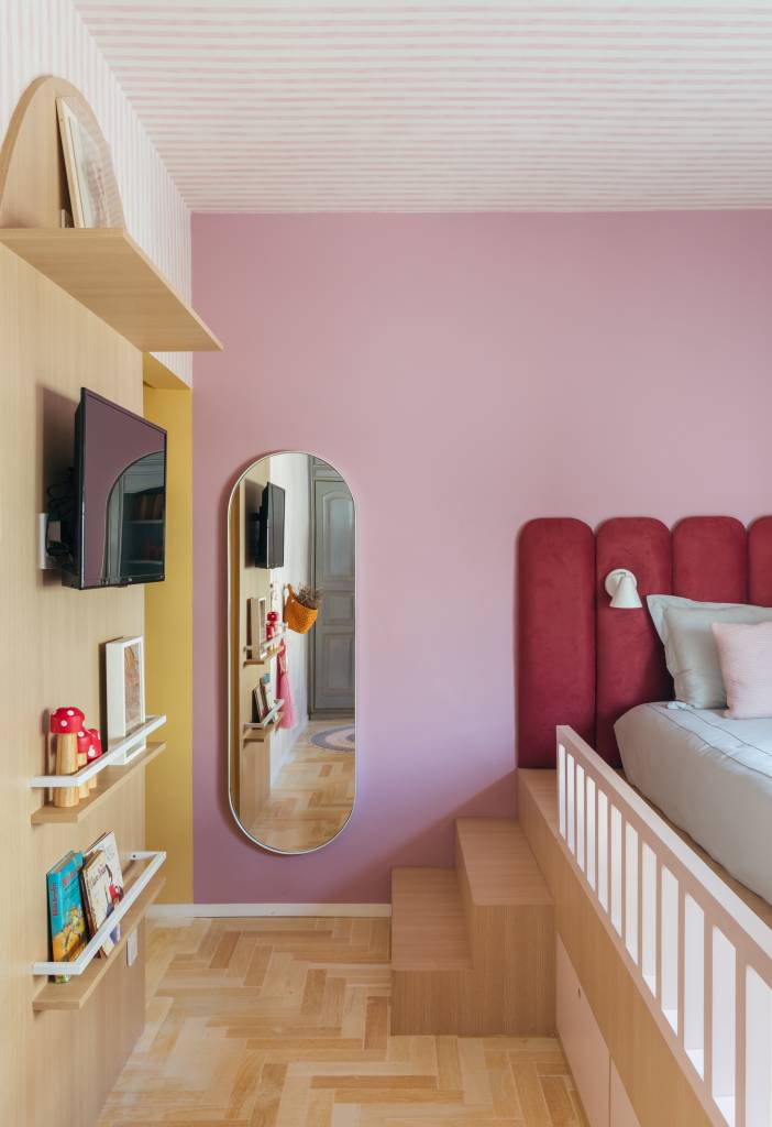 ape-160-m-tons-pastel-alegres-painel-giratorio-tv-gabriela-ikeda-22-quarto-infantil Apê de 160 m² em tons pastel alegres tem painel giratório de TV. Projeto de Ikeda Arquitetura. Na foto, quarto infantil com parede rosa, cabeceira estofada, cama em plataforma com escada, espelho de parede, painel com tv e prateleira para livros.