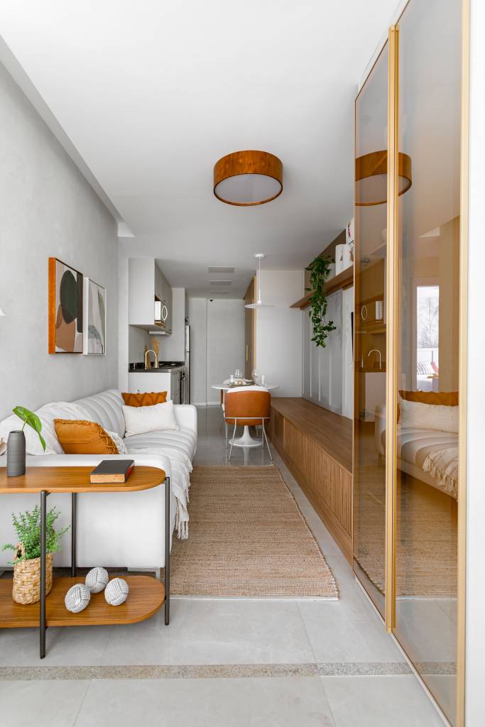 Apê de 56 m² com varanda foi projetado para família de 4 pessoas. Projeto de NOP Arquitetura. Na foto, sala de estar com sofá branco, tapete, mesinha lateral em madeira.