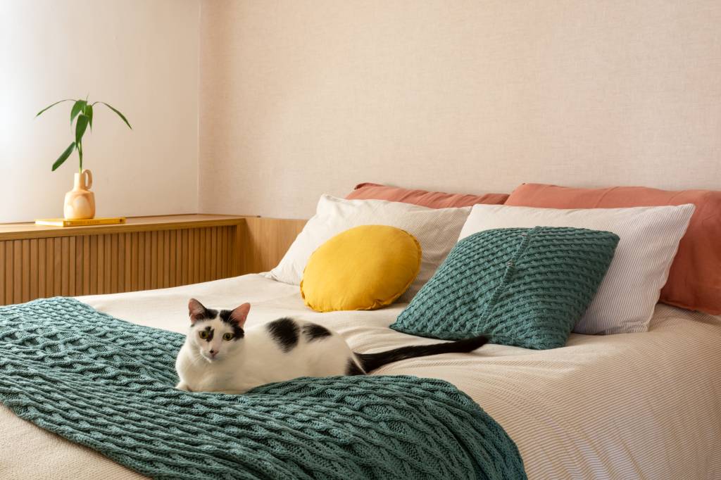 madeira-tom-natural-pintada-de-branco-ape-117-m-mariana-monnerat-taina-binato-07-quarto-gato Madeira em tom natural e pintada de branco dão leveza à apê de 117 m². Projeto de Mariana Monnerat e Tainá Binato. Na foto, quarto de casal com gato em cima de manta da cama.