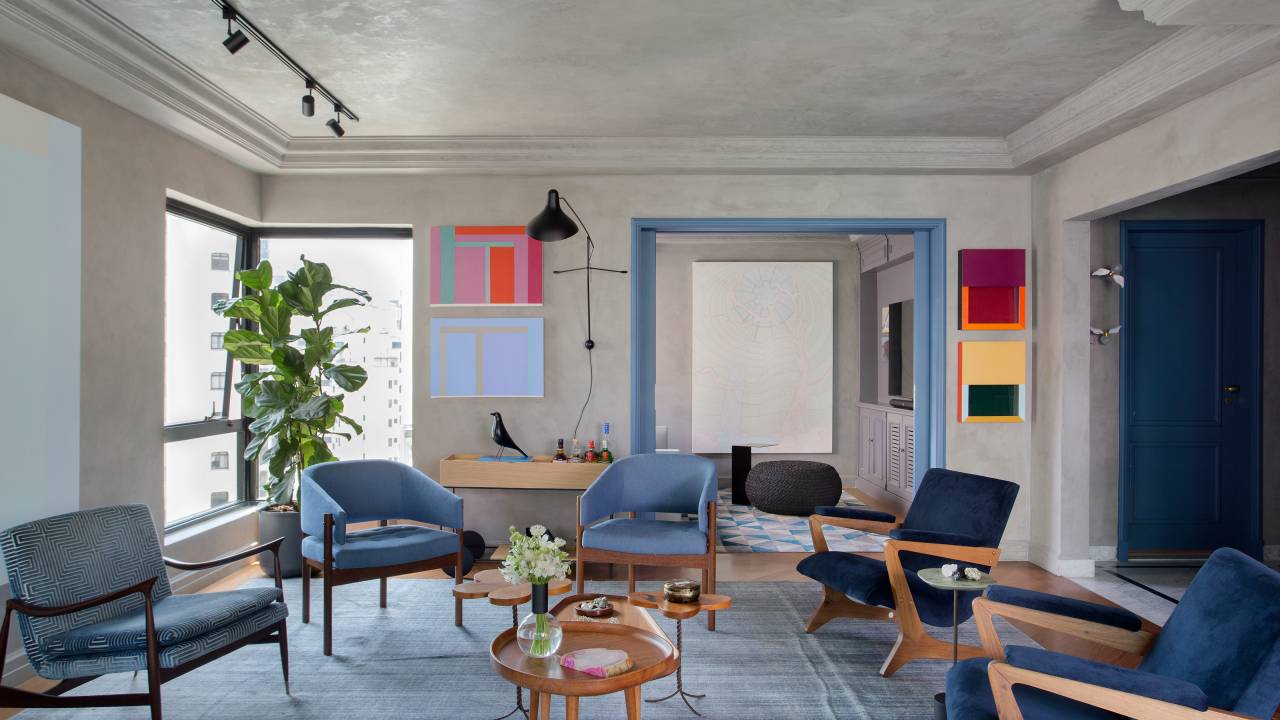 Quadros e cores dão personalidade e charme à apê reformado em 60 dias. Projeto de Ar.Kitekt Associados. Na foto, sala de estar com tapete azul, poltronas azuis, parede e teto revestidos de cimento queimado, quadros.