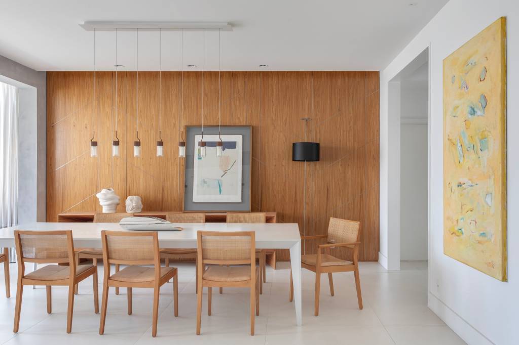 quarto-ape-grande-painel-freijo-natural-laminas-diagonais-cristina-bezamat-13-jantar Quarto deste apê tem grande painel de freijó natural com lâminas diagonais. Projeto de Cristina Bezamat. Na foto, sala de jantar com parede revestida com painel de madeira e mesa grande branca.