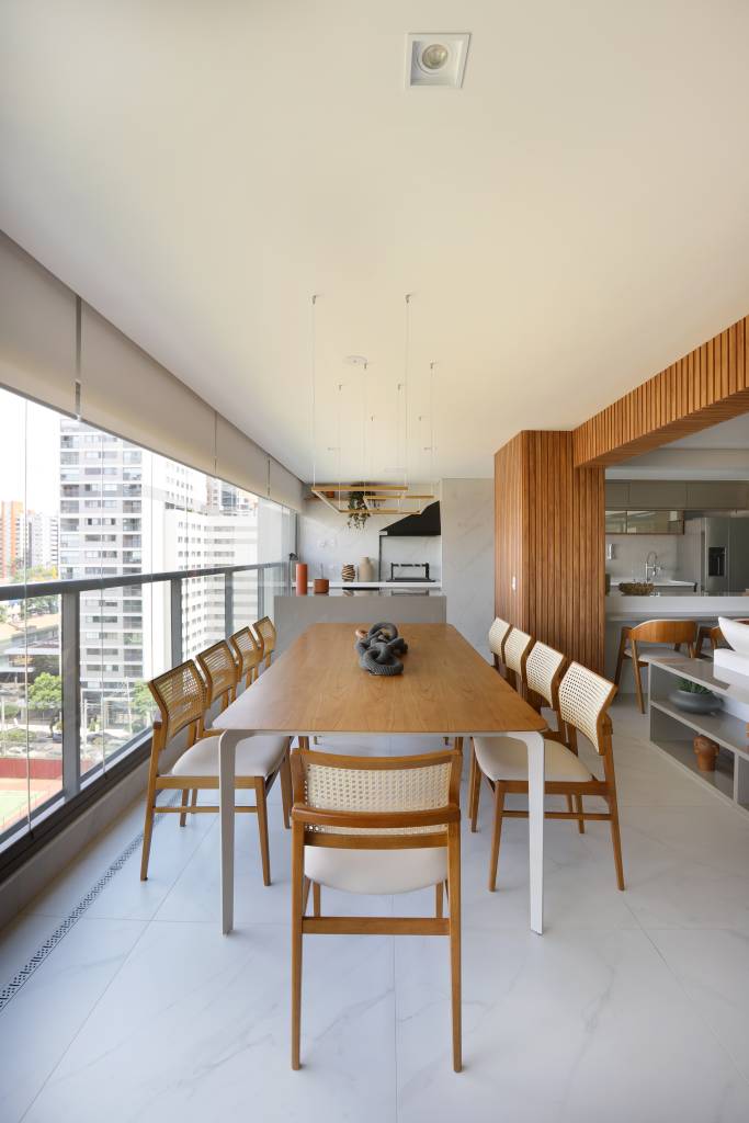 reforma-ape-184-m-elimina-banheiro-ampliar-suite-duno-arquitetura-17-varanda Reforma em apê de 184 m² elimina banheiro para ampliar suíte. Projeto de Duno Arquitetura. Na foto, varanda integrada com mesa grande de madeira, área gourmet ao fundo.