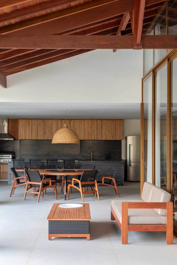 tons-naturais-base-neutra-casa-de-campo-cozinha-provencal-joao-panaggio-08 Tons naturais e base neutra marcam casa de campo com cozinha provençal. Projeto de João Panaggio. Na foto, varanda gourmet com mesa de madeira redonda, bancada preta e marcenaria preta.
