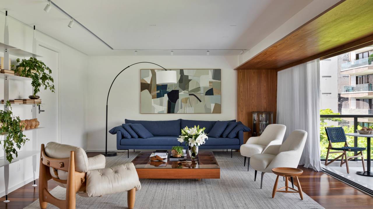 Apê integrado ganha décor contemporâneo com muita marcenaria em freijó. Projeto de João Panaggio. Na foto, sala de estar, sofá azul, quadro, luminária de piso, mesa de centro.