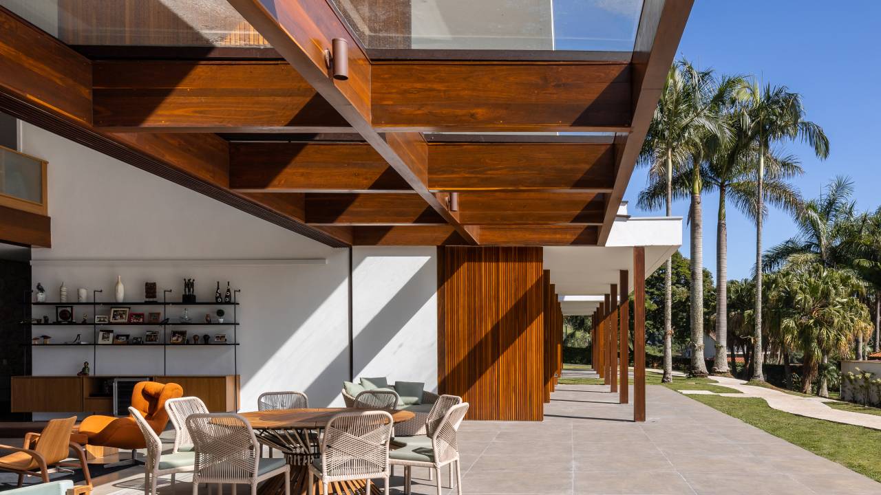 Casa é composta por três volumes ligados por pergolado de madeira. Projeto de Arkitito. Na foto, sala de estar com grandes aberturas, sofá ilha.