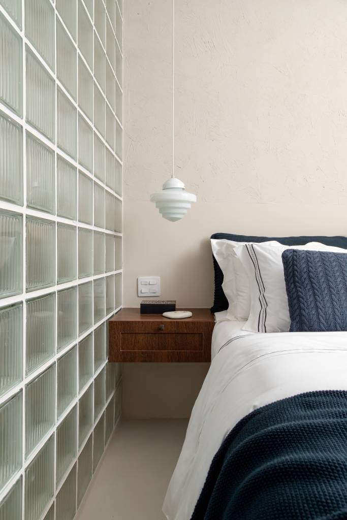 Com 33 m², studio com toque vintage usa tijolos de vidro como divisória. Projeto de Mariana Monnerat. Na foto, quarto com mesa lateral suspensa, parede de tijolos de vidro.