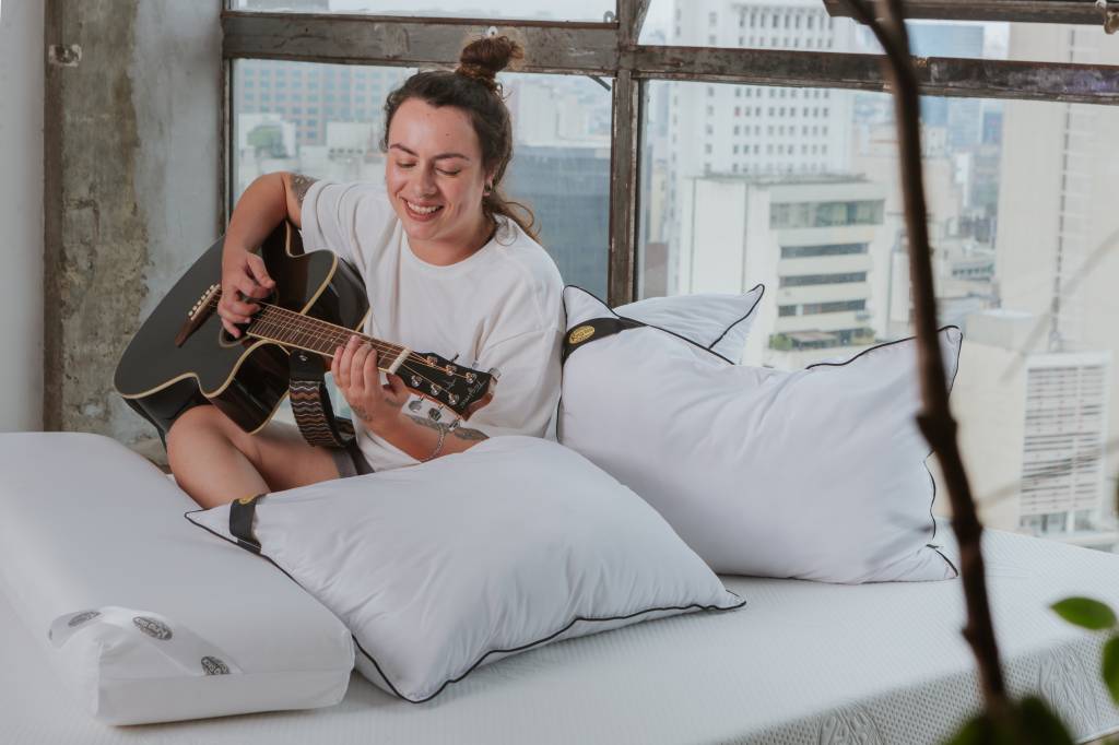 como-escolha-da-cama-influencia-na-decoracao-do-quarto-king-star-13 Como a escolha da cama influencia na decoração do quarto. Na foto, pessoa tocando violão na cama.