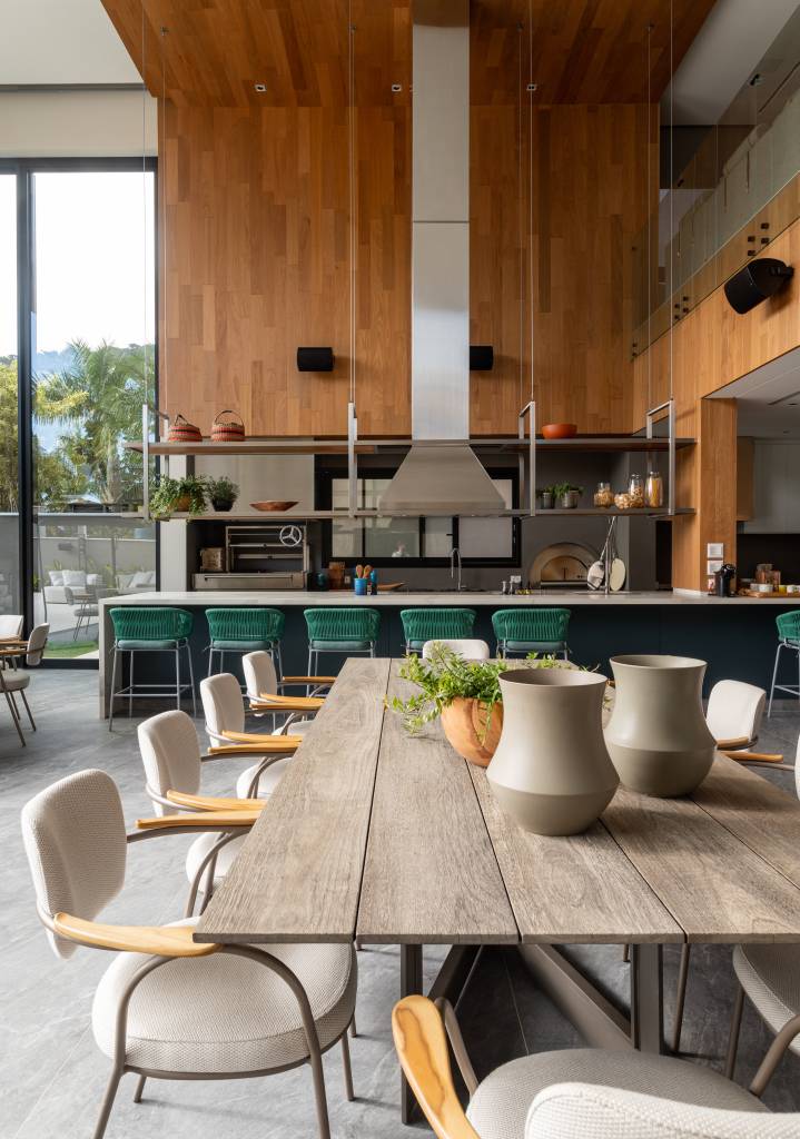 Mix de elementos artesanais, naturais e tecnologia definem casa de praia. Projeto de Patricia Penna. Na foto, cozinha integrada com sala de jantar, mesa rústica de madeira, bancada, banquetas verdes.