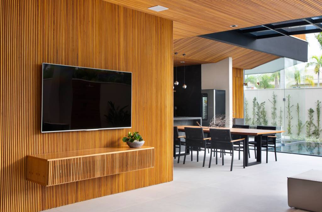 Painéis ripados e área gourmet convidam ao lazer e aconchego nesta casa. Projeto de Studio MH Arquitetura. Na foto, sala de tv, painel ripado, sala de jantar.